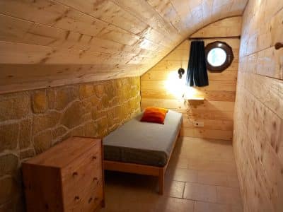 Chalet en bois en Auvergne, avec un lit simple et une fenêtre ronde.