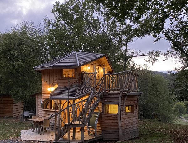 Cabane dans les arbres avec balcons et éclairage chaleureux, entourée de verdure.