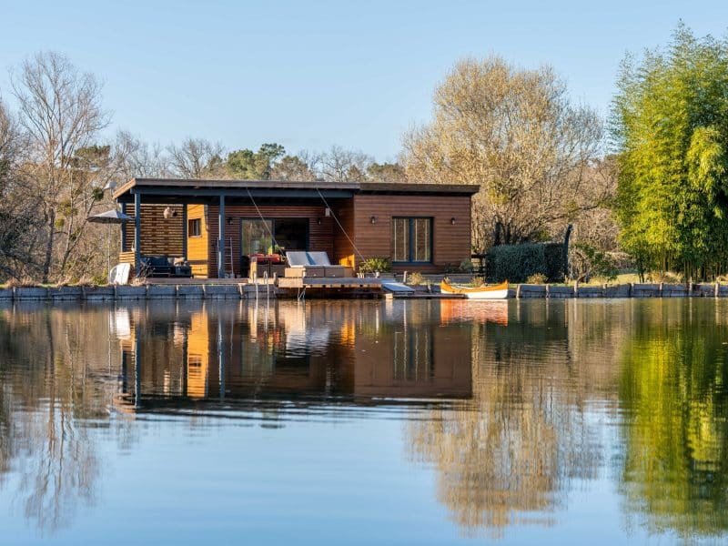 Cabane flottante en Aquitaine, avec terrasse surplombant un lac paisible.