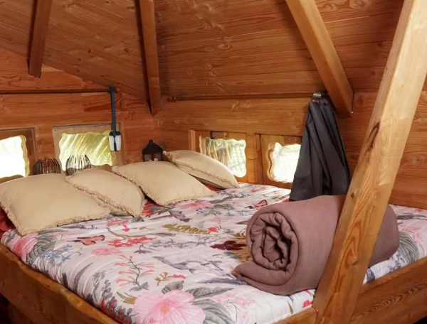 Chalet en bois avec lit douillet et décor floral, ambiance chaleureuse et naturelle.