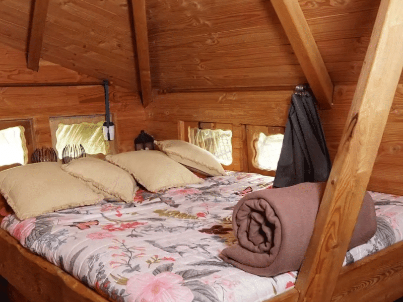 Chalet en bois avec lit douillet et décor floral, ambiance chaleureuse et naturelle.
