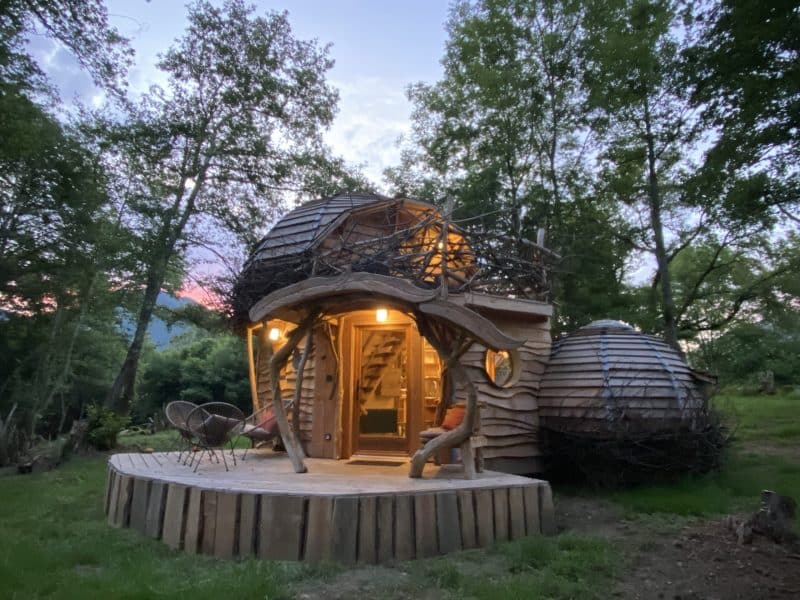 Cabane en bois unique, entourée darbres, avec une terrasse accueillante.