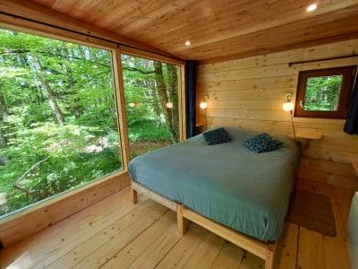Cabane en bois avec grande fenêtre donnant sur la forêt verdoyante en Auvergne.