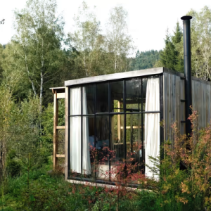 Cabane moderne en bois avec grandes fenêtres, entourée de verdure à Champagne-Ardenne.