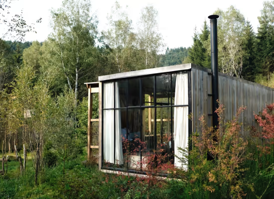Cabane moderne en bois avec grandes fenêtres, entourée de verdure à Champagne-Ardenne.