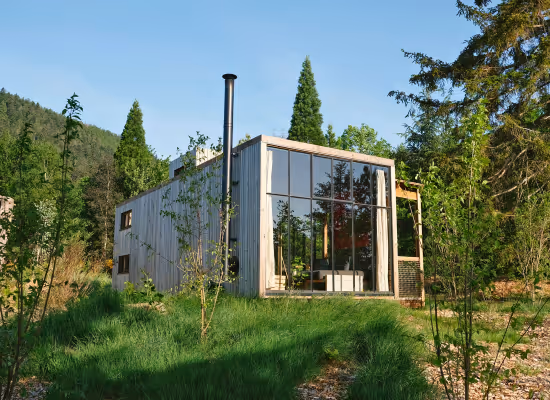Cabane moderne en bois avec grandes baies vitrées, entourée de verdure à Champagne-Ardennes.