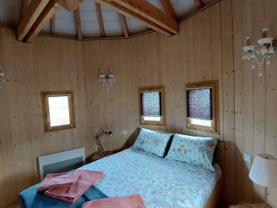 Chalet en bois rond avec lit douillet et fenêtres lumineuses en Auvergne-Rhône-Alpes.