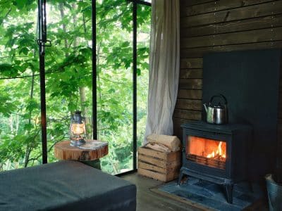 Cabane en bois avec poêle à bois, entourée de verdure apaisante.