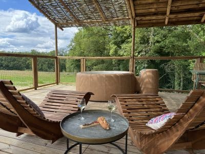 Hébergement insolite en bois avec jacuzzi, chaises longues et vue sur la nature.