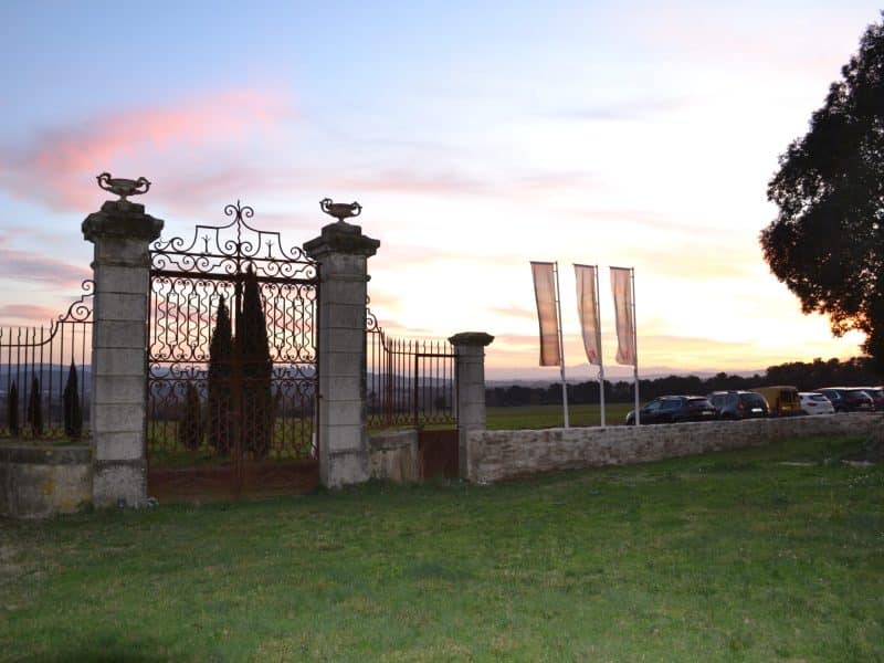 Charmante villa avec portail en fer forgé, entourée de verdure au coucher de soleil.