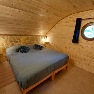 Chalet en bois en Auvergne avec lit double et fenêtre ronde, ambiance chaleureuse.