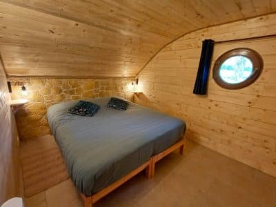 Chalet en bois en Auvergne avec lit double et fenêtre ronde, ambiance chaleureuse.