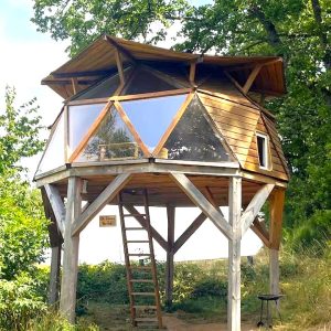 Cabane perchée en bois avec grandes fenêtres, entourée de verdure en Auvergne.