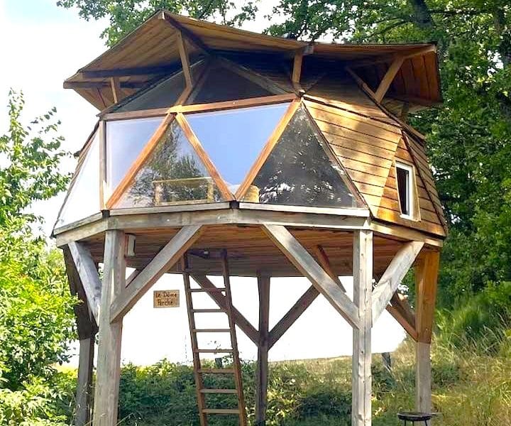 Cabane perchée en bois avec grandes fenêtres, entourée de verdure en Auvergne.