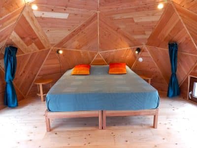 Hébergement insolite en Auvergne : cabane en bois avec un lit confortable et des coussins colorés.