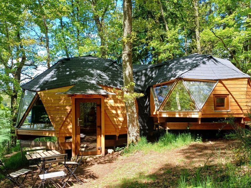 Cabane en bois moderne, entourée darbres, avec grandes baies vitrées.