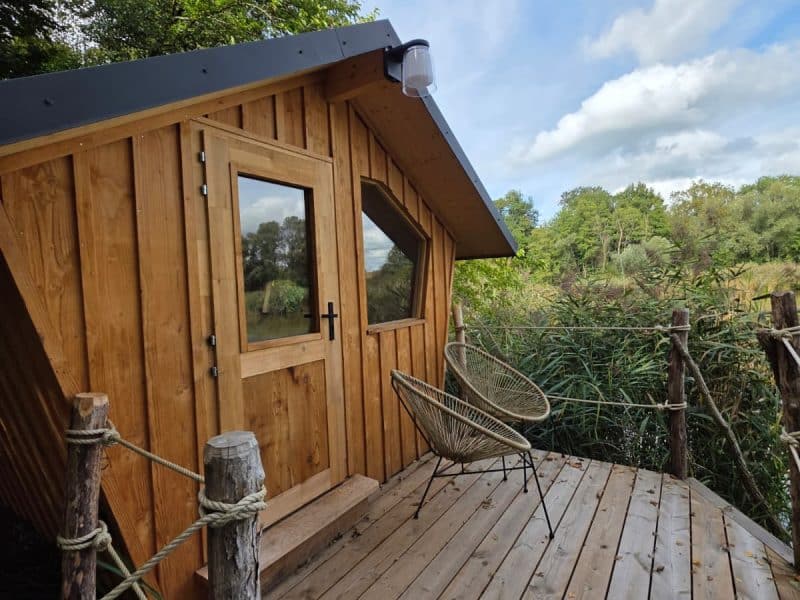 Cabane en bois perchée sur pilotis, avec terrasse et vue sur la nature environnante.