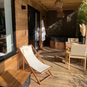 Chalet en bois avec terrasse, fauteuil relaxant et jacuzzi en extérieur.