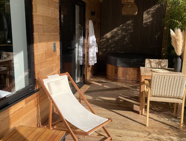 Chalet en bois avec terrasse, fauteuil relaxant et jacuzzi en extérieur.