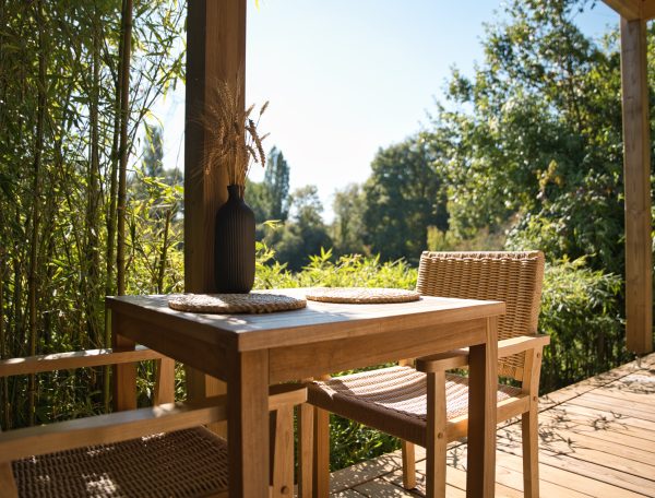 Chalet en bois avec terrasse, table en bois et vue sur la nature verdoyante.