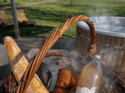 Panier gourmand avec pain et boissons près dun jacuzzi dans un hébergement insolite.