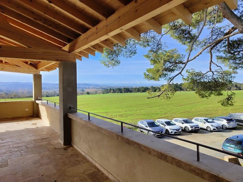Terrasse dun gîte moderne avec vue sur des champs verdoyants et voitures stationnées.