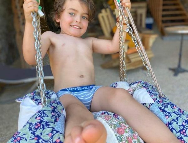 Un gîte rural avec un enfant souriant sur une balançoire en tissu coloré.