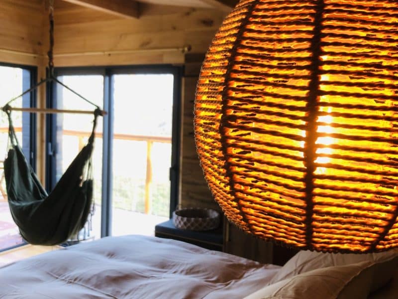 Chambre chaleureuse avec lit douillet et lampe en rotin suspendue.