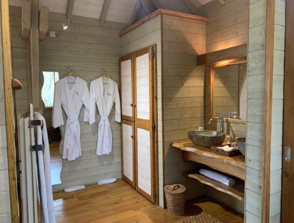 Cabane en bois avec salle de bain élégante et peignoirs suspendus.