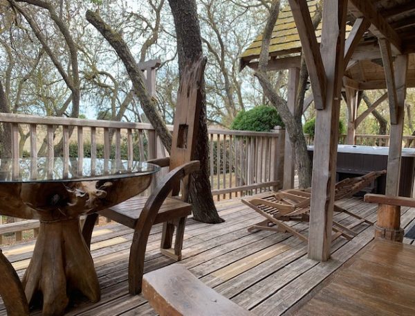 Cabane en bois avec terrasse, table en bois et chaises longues sous les arbres.