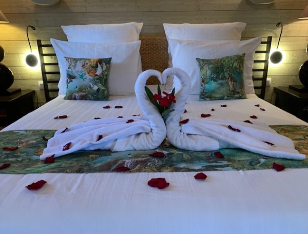 Chambre romantique avec lit décoré de serviettes en forme de cygnes et pétales de roses.