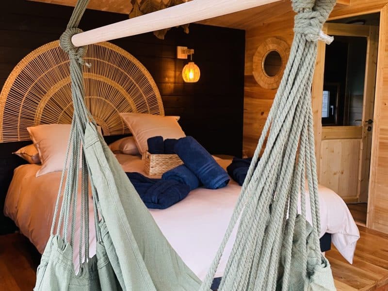 Chalet cosy avec hamac suspendu et lit douillet, ambiance chaleureuse et bois naturel.
