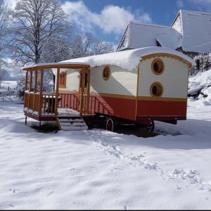 Charmante roulotte en bois, entourée de neige, avec un balcon en bois.