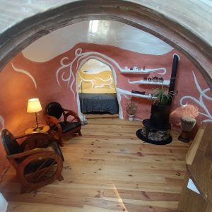 Hébergement insolite en forme de cabane, intérieur coloré avec un poêle et des fauteuils en bois.