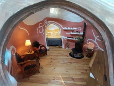 Hébergement insolite en forme de cabane, intérieur coloré avec un poêle et des fauteuils en bois.