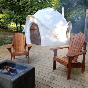Hébergement insolite en forme de dôme, avec chaises en bois et feu de camp.