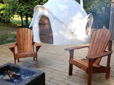 Hébergement insolite en forme de dôme, avec chaises en bois et feu de camp.