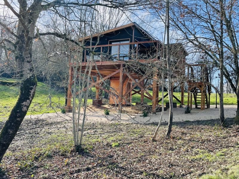 Cabane sur pilotis entourée darbres, offrant un cadre naturel paisible.