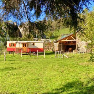Charmante roulotte en bois, entourée de verdure et de collines verdoyantes.