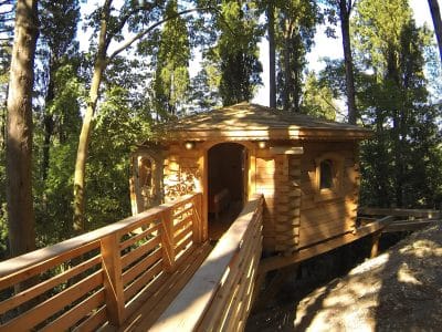 Cabane perchée en bois, entourée darbres, avec une terrasse en bois accueillante.