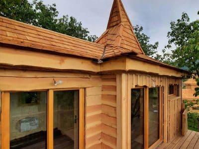 Cabane en bois avec toit en pointe, entourée de verdure en Auvergne-Rhône-Alpes.