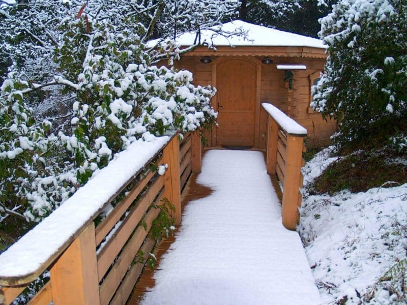 Chalet en bois entouré de neige, avec un chemin en bois menant à la porte.
