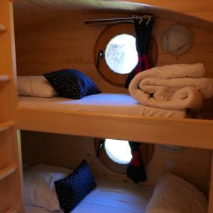 Chalet douillet avec lits superposés et fenêtres rondes, ambiance chaleureuse en bois.