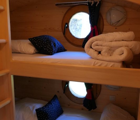 Chalet douillet avec lits superposés et fenêtres rondes, ambiance chaleureuse en bois.