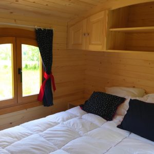 Chalet en bois cosy avec lit douillet et vue sur la nature à travers une fenêtre.