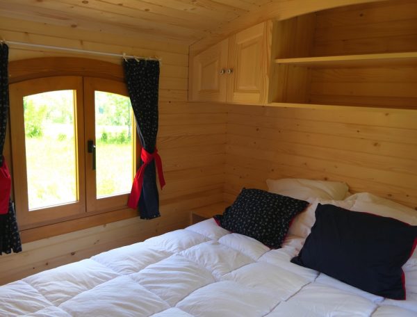 Chalet en bois cosy avec lit douillet et vue sur la nature à travers une fenêtre.
