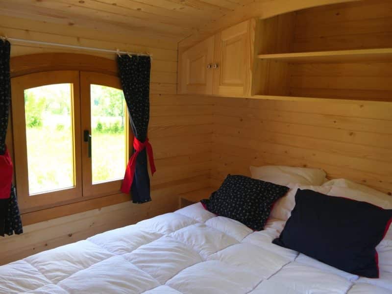 Chalet en bois cosy avec lit douillet et vue sur la nature à travers une fenêtre.