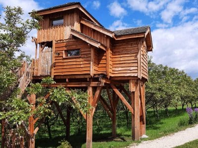 Cabane perchée en bois, entourée darbres, offrant une vue imprenable sur la nature.