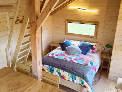 Cabane en bois avec lit douillet et décoration colorée, située en Auvergne-Rhône-Alpes.