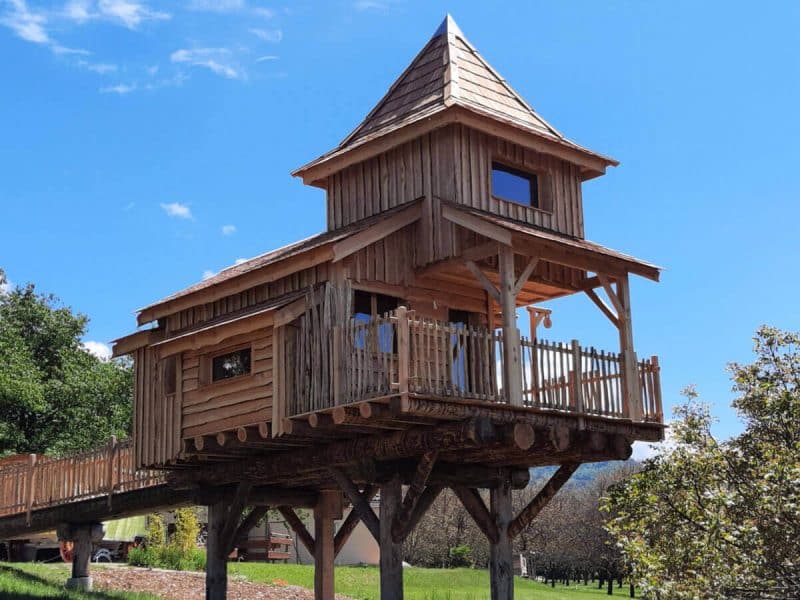 Cabane perchée en bois avec toit en pente, entourée de verdure en Auvergne-Rhône-Alpes.